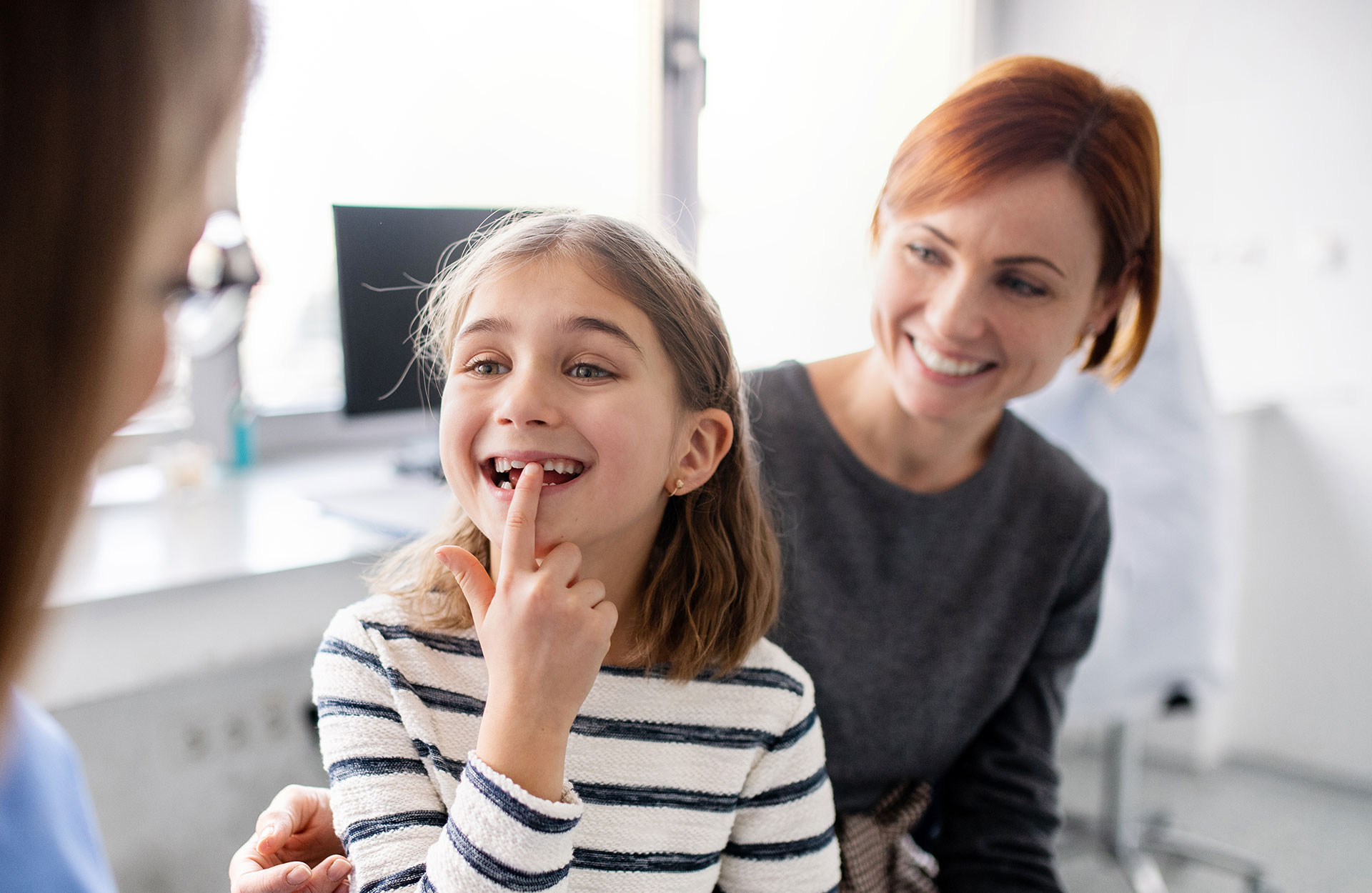 A young girl in a dental office with her mouth open, receiving a dental check-up while seated on a chair, under the supervision of a dentist.