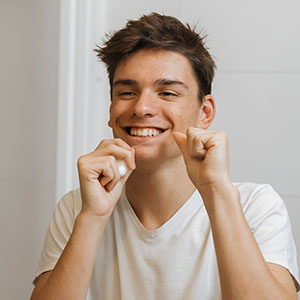A young man with short hair, smiling broadly, holding his cheeks with both hands.