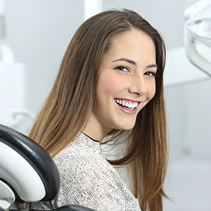 A young woman with a wide smile is sitting in a dental chair, likely at a dentist s office.